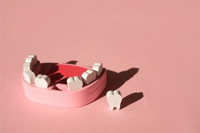 Wooden set of teeth with one removed to leave a gap on a pink background