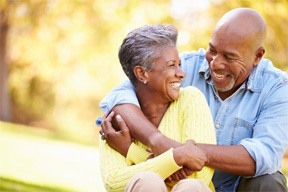 Bald man with white beard hugging woman in yellow sweater outside smiling