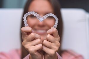 Woman holding clear aligners toward the camera in the shape of a heart