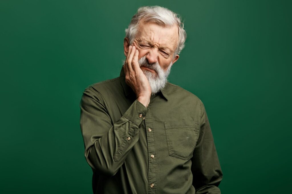 An older man holding his jaw in pain.