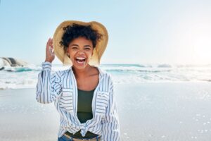 Woman in striped shirt and straw hat at the beach laughing