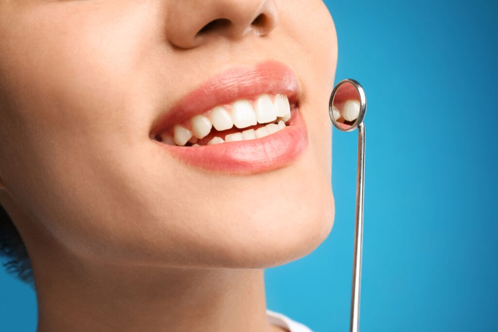 Nose-to-chin view of woman smiling with dental mirror held up in front of light blue background